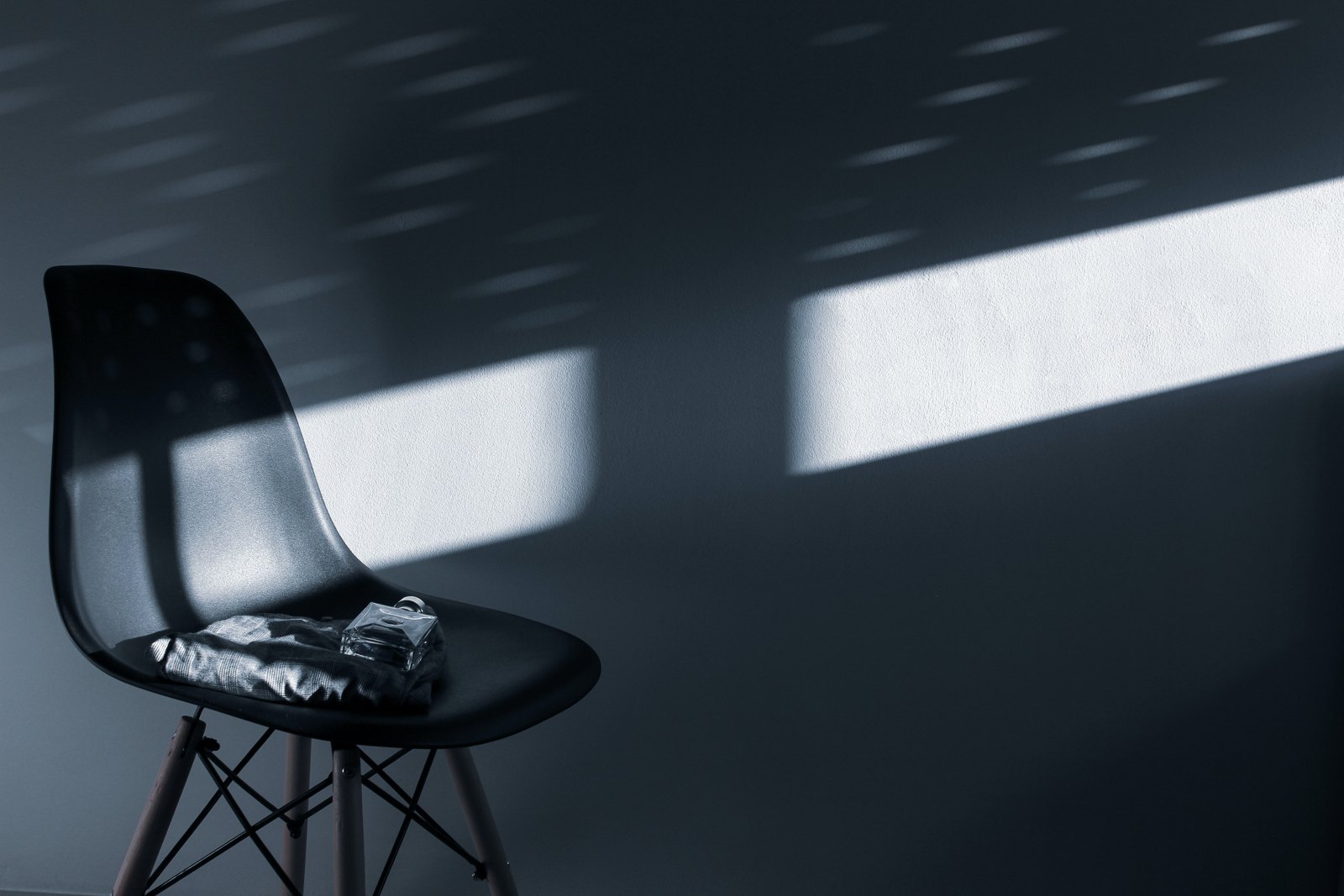 An empty dark chair against a wall cut by hard window light