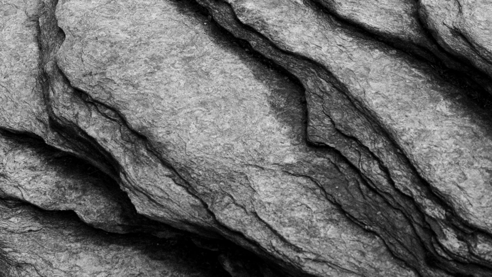 Close up of dark layered rock strata, thick bands separated by thin seams