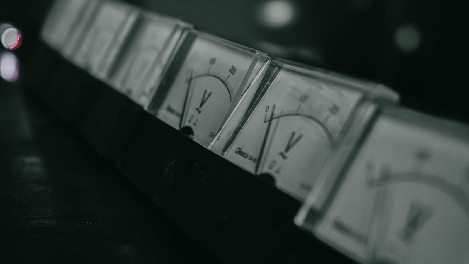 A row of vintage analog voltage meters in a dark industrial setting