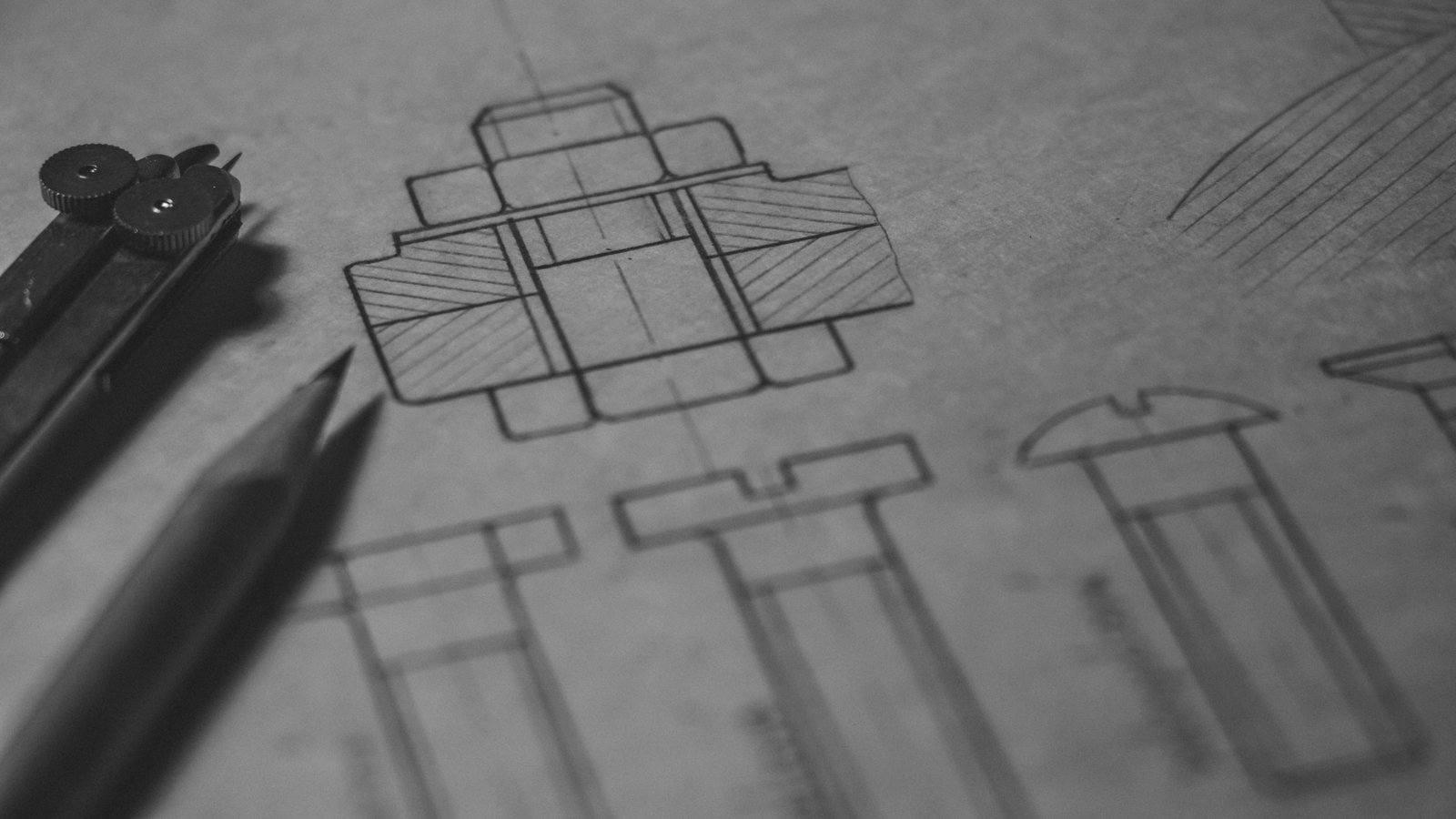 A black and white engineering drawing of bolts and a cross section, with a pencil and dividers resting on the paper