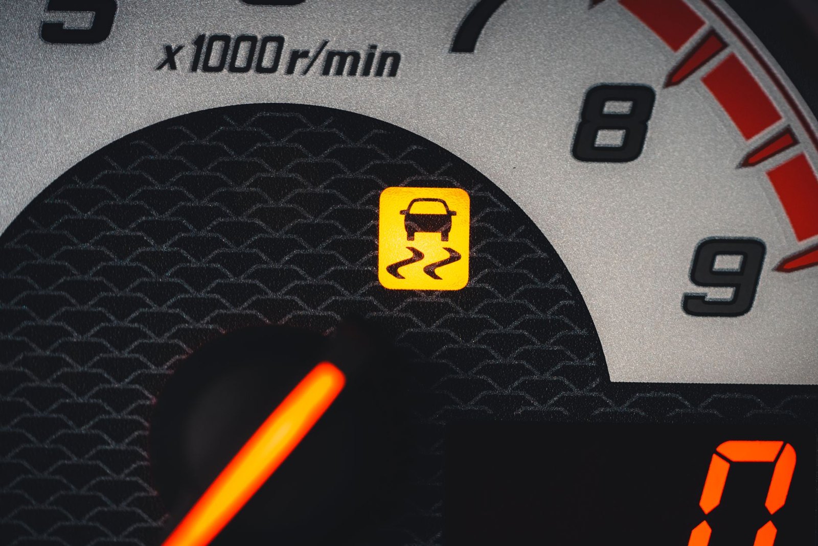 Close up of a dark instrument cluster with a single amber traction warning light lit beside the dial markings