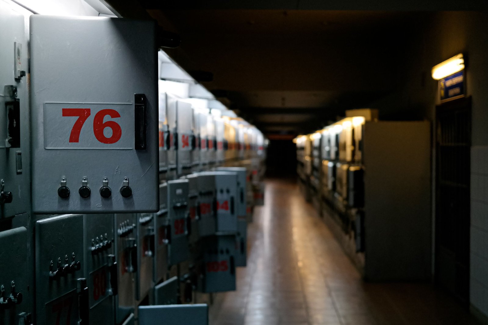 A dim corridor of numbered electrical switchgear cabinets with a single light at the far end